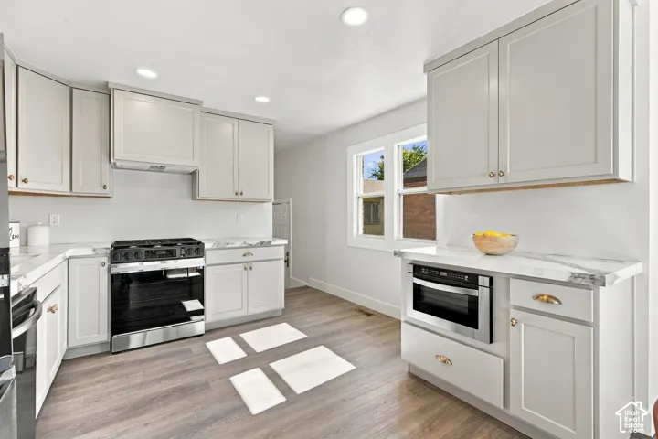 Kitchen featuring light-toned shaker cabinetry, stone-patterned countertops, wood-finish flooring, recessed lighting, and stainless steel appliances