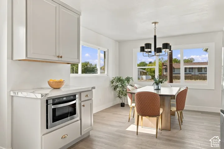 Dining area featuring wood-finish flooring, shaker-style cabinetry with integrated microwave, stone-surface countertop, and a multi-arm chandelier