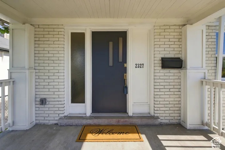 Covered front porch featuring white-painted brick exterior, central door with vertical glass insets, sidelight window, and box column supports