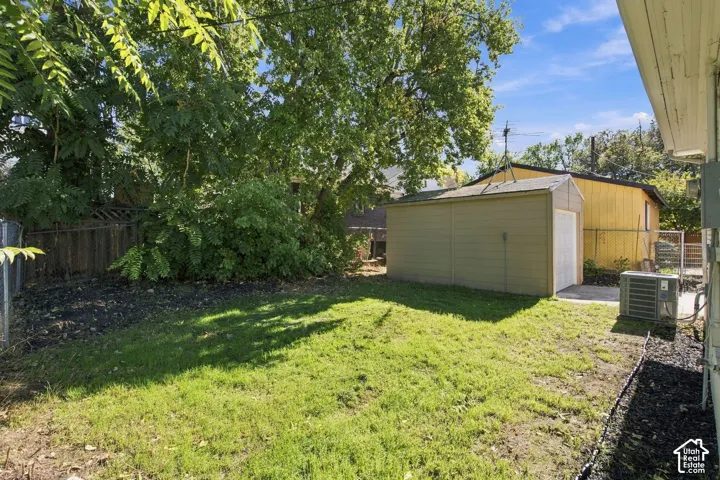 Backyard space featuring a detached storage structure, lawn area, mature trees, and perimeter fencing