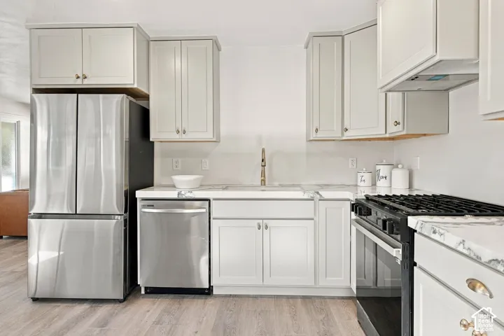 Kitchen featuring light-toned cabinetry, stone-finish countertops, stainless steel appliances, and wood-finish flooring