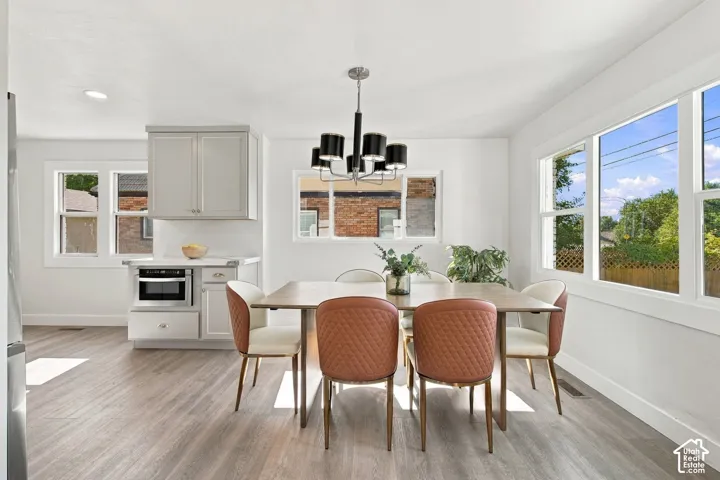 Dining area featuring wood-finish flooring, light grey built-in cabinetry with a microwave, multi-arm chandelier, and expansive windows