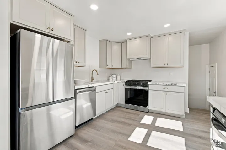 Kitchen featuring light-toned cabinetry, stone-finish countertops, stainless steel appliances, and wood-finish flooring