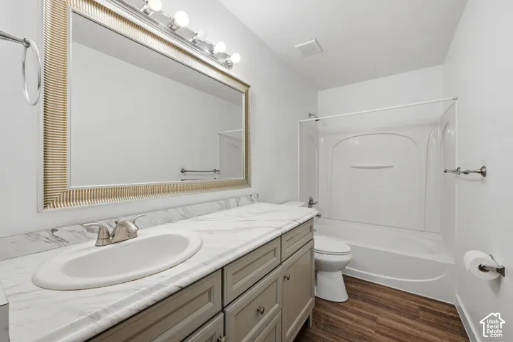 Bathroom featuring vanity with stone-patterned countertop, oval undermount sink, framed wall-mounted mirror, wood-finish flooring, and tub-shower combination