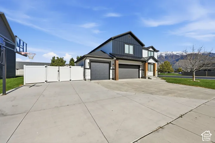 Modern two-story exterior featuring a metal and composite roof, dark vertical siding, stone masonry accents, three-car garage, and an expansive concrete driveway