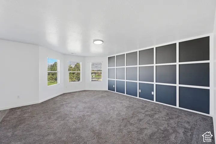 Spacious room featuring a decorative grid-patterned accent wall, neutral carpeting, three large windows, and a flush-mount ceiling light fixture