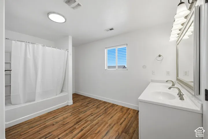 Bathroom featuring a dual-sink vanity with a large mirror, wood-finish flooring, and a combined tub and shower unit