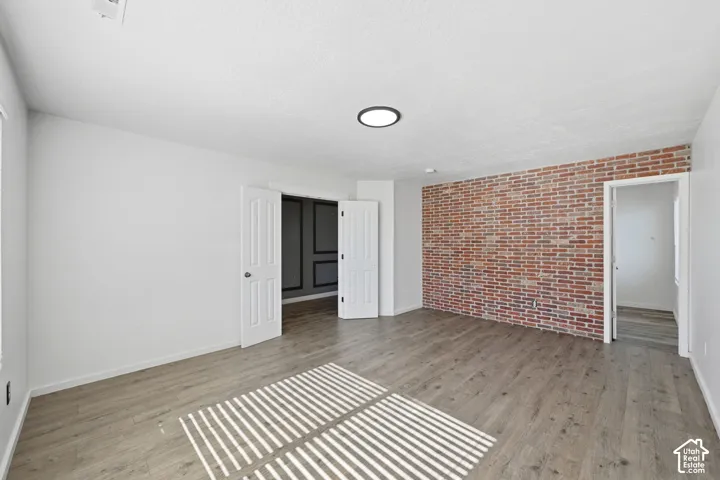 Room featuring an exposed brick accent wall, wood-finish flooring, and recessed ceiling lighting