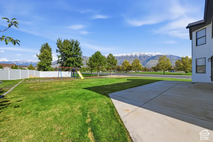 Concrete patio, expansive lawn, white vinyl fencing, and mountain backdrop