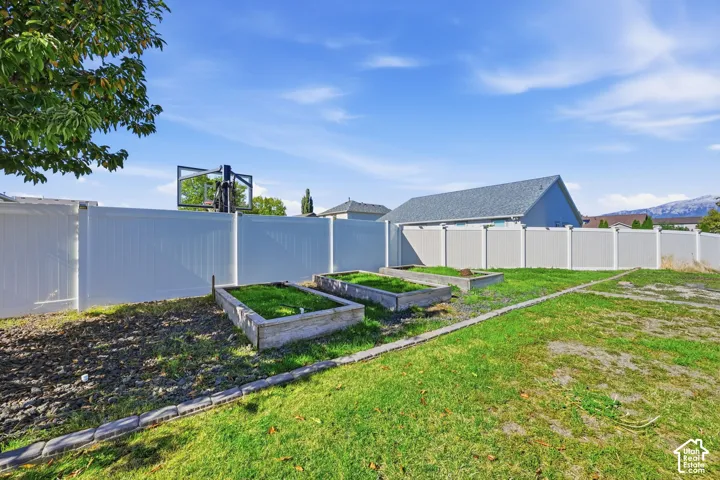 Backyard featuring a white vinyl privacy fence, raised wooden garden beds, and stone perimeter edging