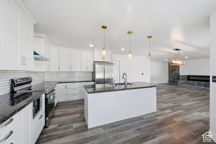 Kitchen featuring white shaker-style cabinetry, stone countertops, subway tile backsplash, center island with shiplap detailing, and wood-finish flooring
