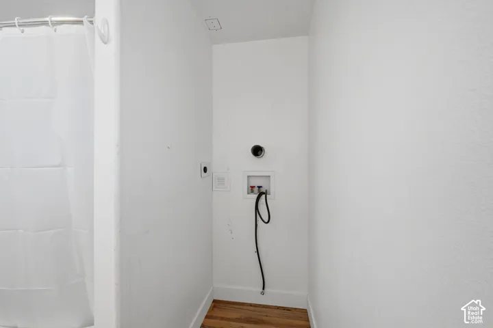 Laundry alcove featuring a recessed water supply box, dedicated drainage line, and wood-finish flooring