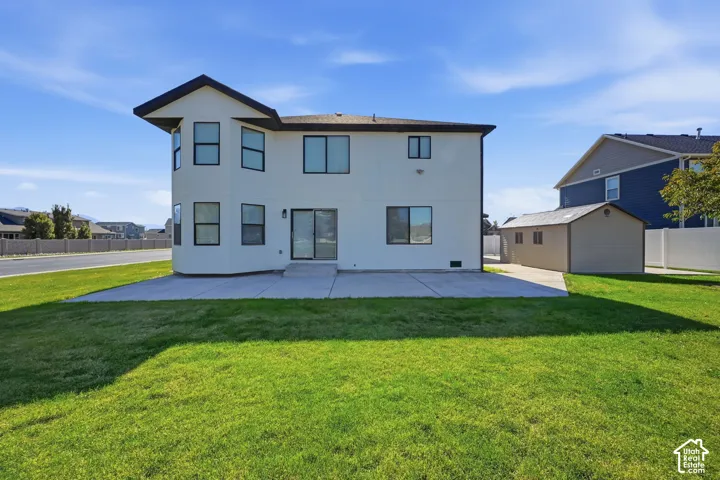 Rear exterior featuring a two-story stucco facade, concrete patio, multi-faceted bay window, and detached storage shed situated on a lawn