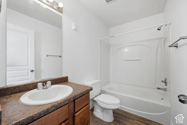 Bathroom featuring wood-finish cabinetry, stone-texture countertop with integrated oval sink, full-width vanity mirror, and a tub-shower combination with a molded surround