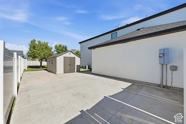 Concrete side yard featuring a white vinyl privacy fence, detached storage shed, and stucco exterior finish