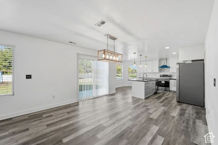 Open-concept area featuring wood-finish flooring, a kitchen island with stone-finish countertops, stainless steel appliances, and a modern rectangular pendant light fixture