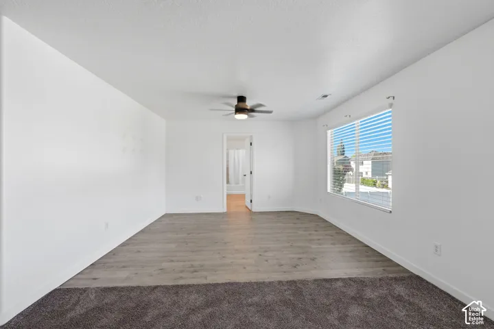 Spacious room featuring wood-finish flooring, neutral wall paint, a ceiling fan with integrated lighting, and a large window with horizontal blinds