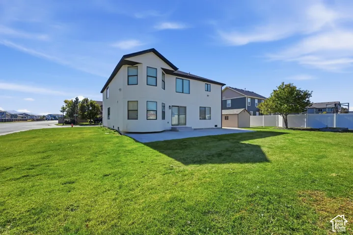 Two-story exterior featuring light-toned stucco siding, a concrete rear patio, large windows, and a fully fenced backyard