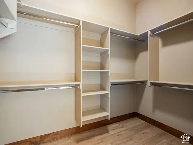 Walk-in closet featuring multi-tiered hanging rods, integrated shelving units, wood-finish flooring, and solid-surface shelving