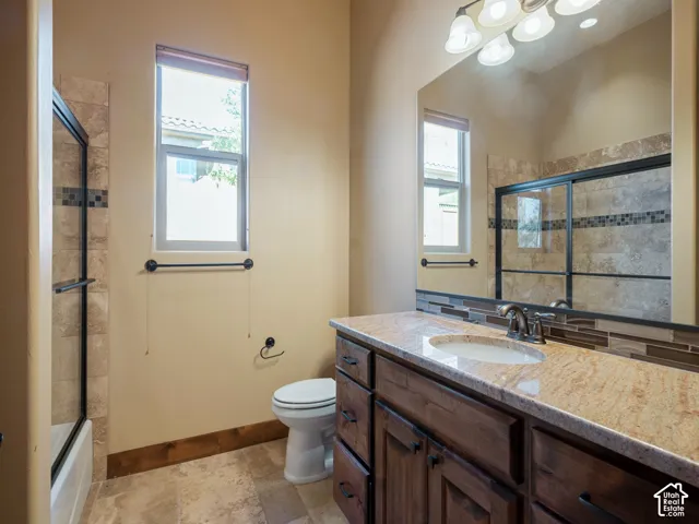 Bathroom featuring a wood vanity with stone countertop, stone-tiled shower surround with decorative glass accent trim, large wall-mounted mirror, and stone flooring