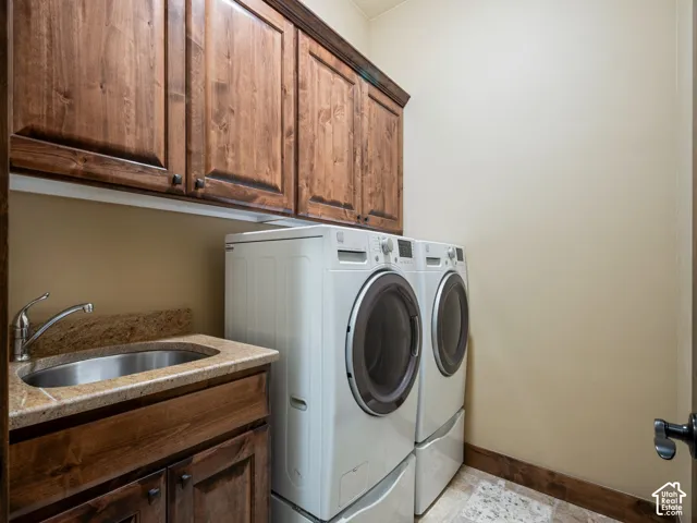 Laundry space featuring stained wood cabinetry, natural stone countertops, an integrated stainless steel basin with a chrome faucet, and tile flooring