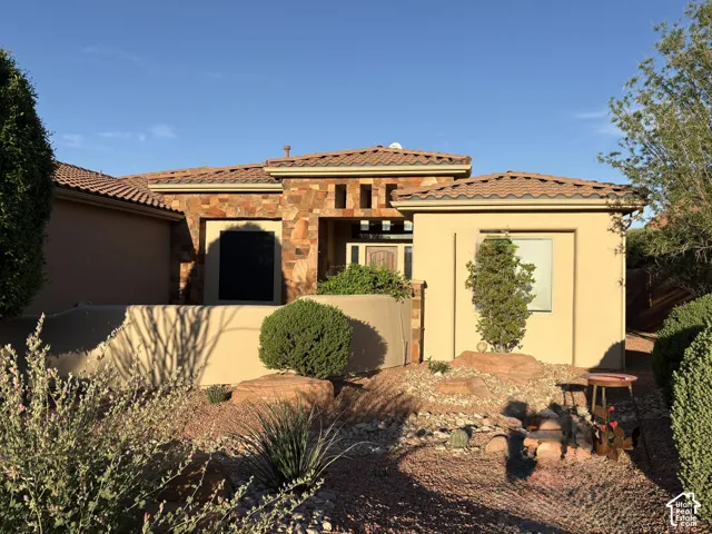 Stucco exterior with natural stone facade, tile roof, and xeriscaped front yard featuring rock landscaping