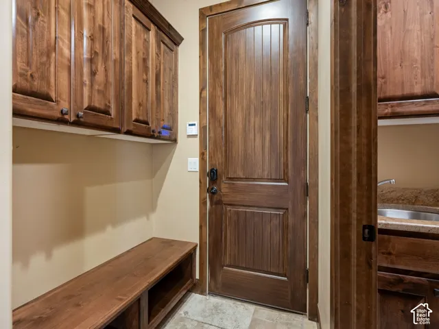 Stained wood cabinetry, built-in wooden bench with open storage, solid wood door with vertical panel detailing, stone tile flooring, and integrated countertop with basin