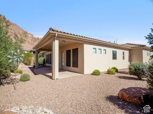 Stucco exterior with a tiled roof, featuring a covered concrete patio, desert landscaping, and prominent mountain backdrop