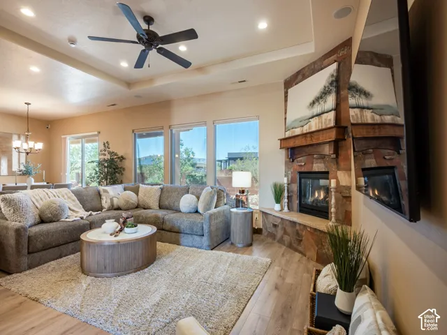 Corner stone fireplace with a wooden mantel, tray ceiling, recessed lighting, ceiling fan, and wood-finish flooring