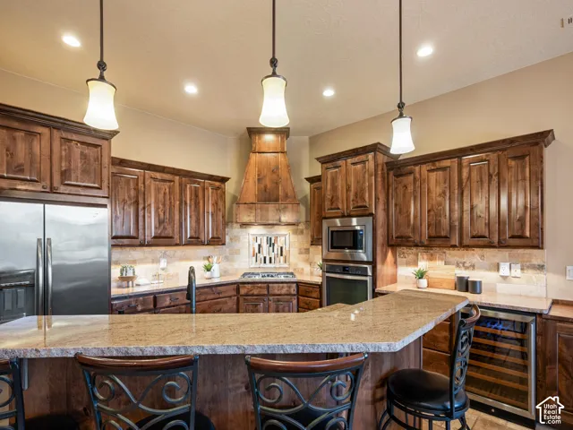Kitchen featuring stained wood cabinetry, stone-surface countertops, custom wood-encased range hood, built-in stainless steel double oven, and pendant lighting