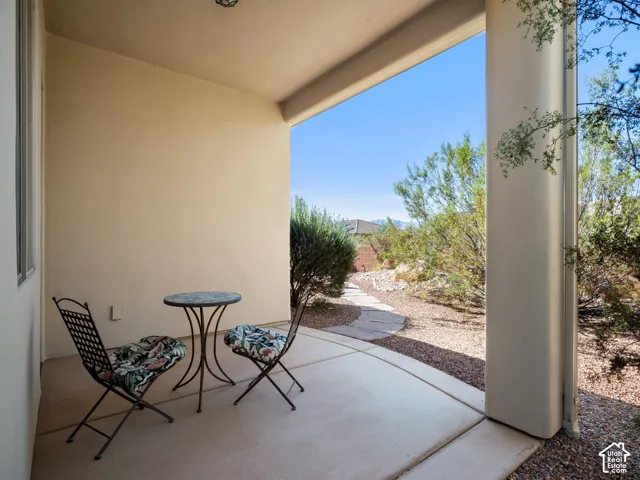 Covered concrete patio featuring smooth stucco wall finish, structural pillar, stone paver pathway, and desert landscaping