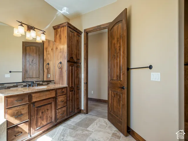 Stained wood cabinetry, stone-finish vanity countertop, large wall-mounted mirror, multi-light vanity fixture, and tile flooring
