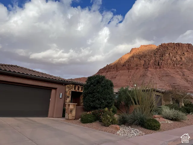 Stucco exterior featuring stacked stone accents, concrete driveway, tiled roof, and desert-inspired landscaping against a mountain backdrop
