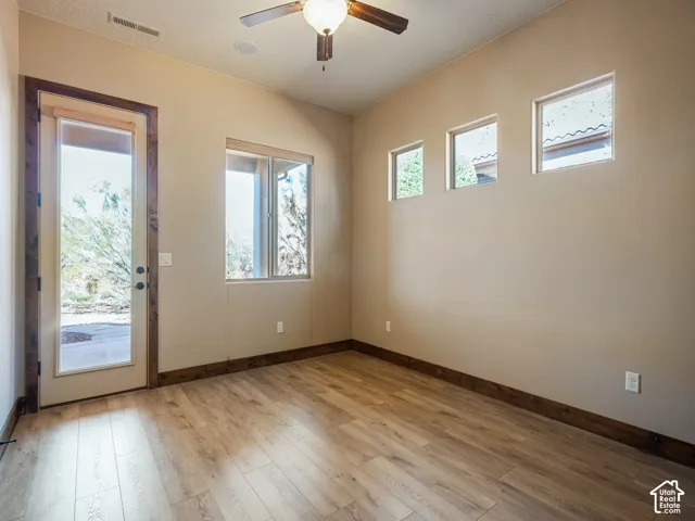 Wood-finish flooring, dark wood door and window casing, three square clerestory windows, exterior glass-paneled door, and a ceiling-mounted light fixture with fan