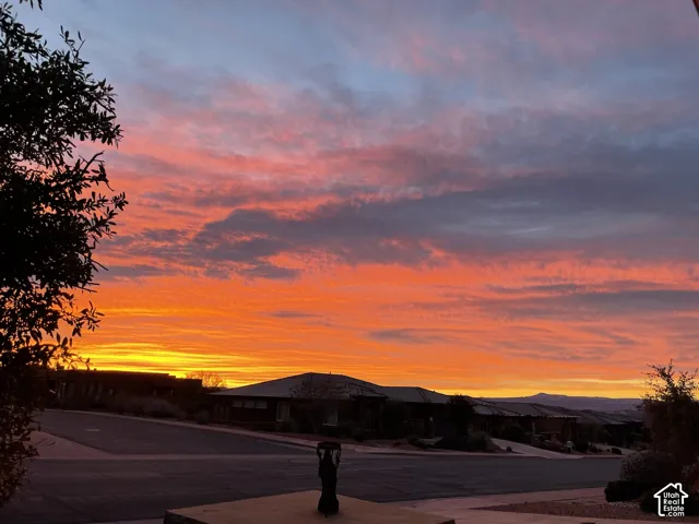 Vibrant sunset backdrop over a residential street with dark-toned single-story architecture and mature desert landscaping