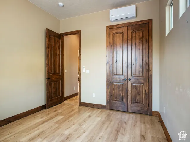 Wood-finish flooring, solid wood doors with arched detailing, dark stained wood trim, and a wall-mounted ductless heating and cooling unit