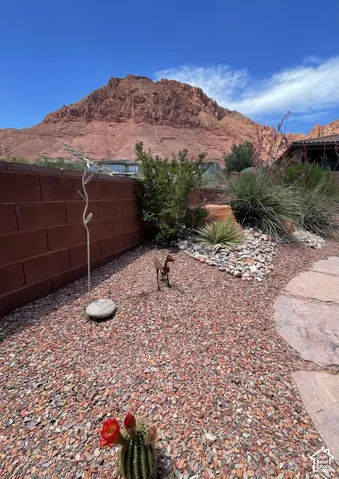Xeriscaped grounds featuring red crushed stone, stone pavers, decorative masonry wall, native desert flora, and prominent mountain backdrop