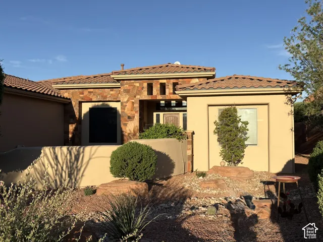 Stucco exterior featuring stacked stone masonry, a clay tile roof, and a walled courtyard entrance