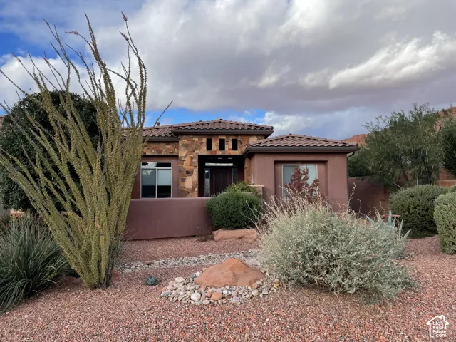 Exterior facade featuring textured stucco walls, stacked stone accents, and a tile roof, complemented by desert-inspired landscaping with rock ground cover and indigenous vegetation