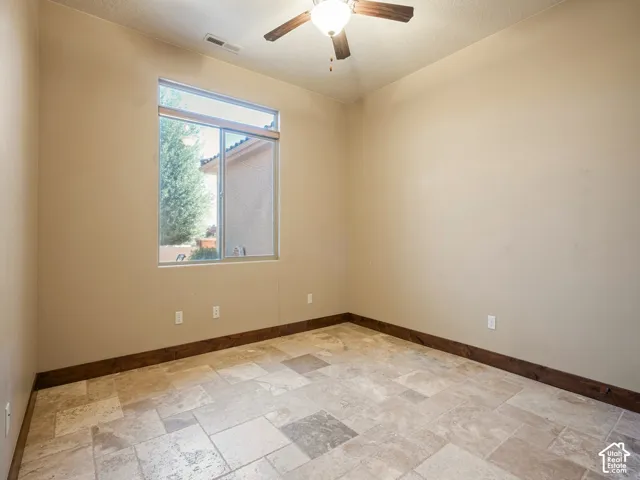Neutral-toned interior room featuring large-format tile flooring, dark wood-finish trim, a single-pane sliding window, and a ceiling fan with integrated lighting