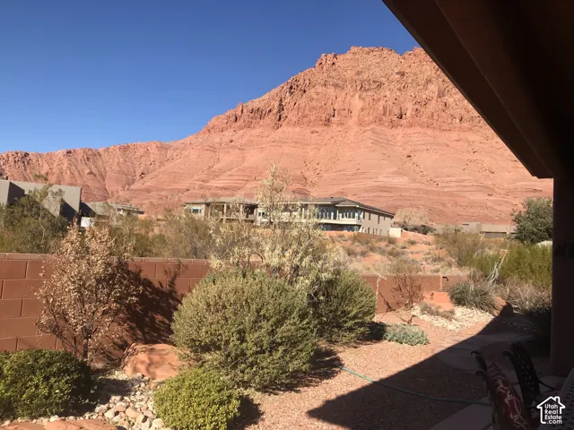 Covered patio overlooking prominent red rock mountain formations, xeriscaped ground cover, stone masonry perimeter wall, and mature desert vegetation