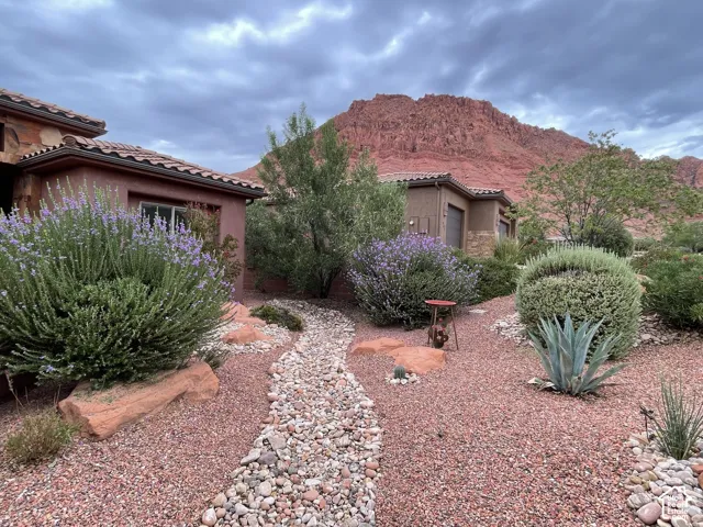Stucco exterior featuring tile roofing, stone accents, and native desert landscaping with a rock-lined pathway set against a red rock mountain backdrop