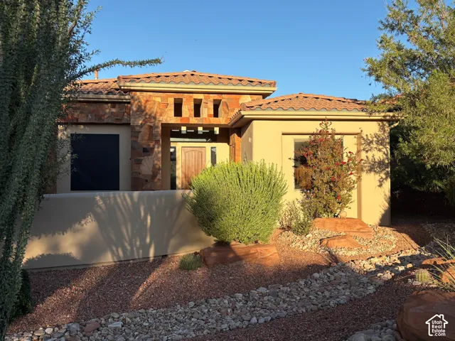 Stucco exterior featuring stacked stone accents, tile roofing, and xeriscaped front grounds with a natural stone pathway