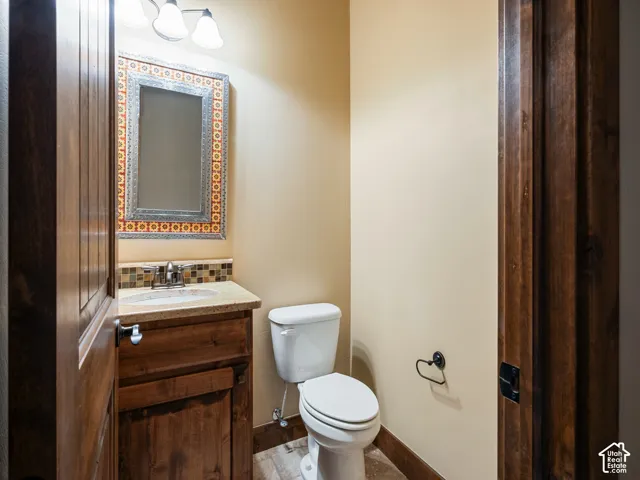 Powder room featuring a wood vanity with a stone-surface countertop, an inset sink with a chrome faucet, a decorative tiled backsplash, and a framed mirror with integrated lighting