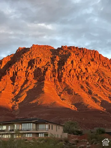 Two-story residence featuring expansive floor-to-ceiling windows, wrap-around balcony, and exterior stucco finish, set against a prominent red rock mountain backdrop