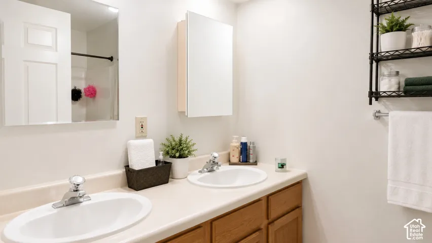 Double vanity featuring solid-surface countertops, integrated oval basins, polished chrome hardware, and wood-finish cabinetry, complemented by a mirrored medicine cabinet and wall-mounted towel bar