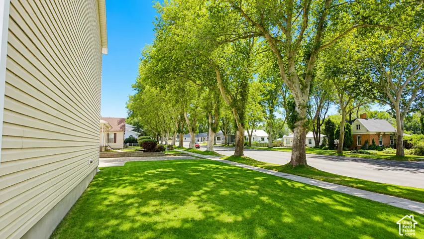 Exterior featuring light-colored horizontal siding, manicured grass lawn, and mature canopy trees