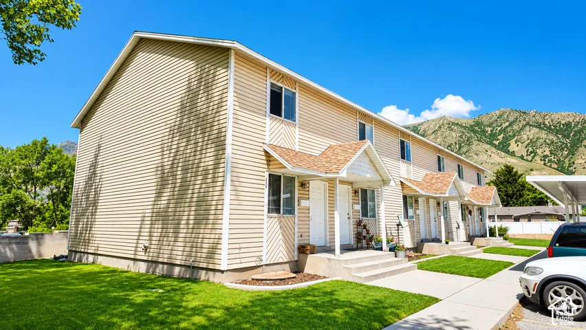 Two-story exterior featuring tan horizontal siding, gable-roofed entryways with asphalt shingles, concrete stairs, and mountain backdrop