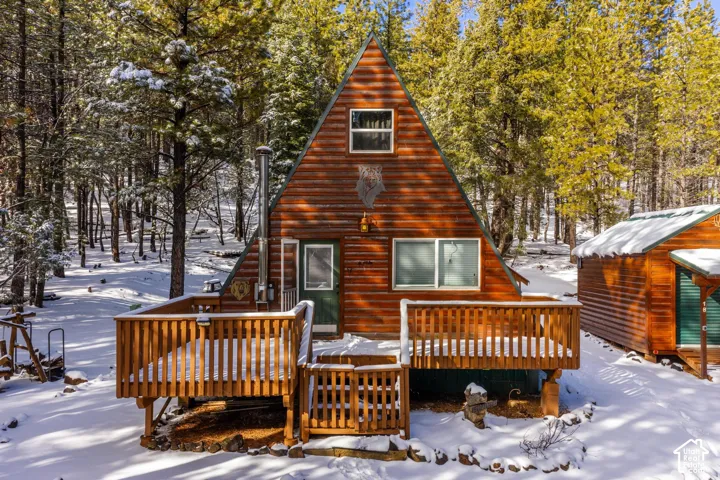 A-frame exterior featuring wood siding, an elevated wrap-around deck with wood railings, and an exterior metal chimney