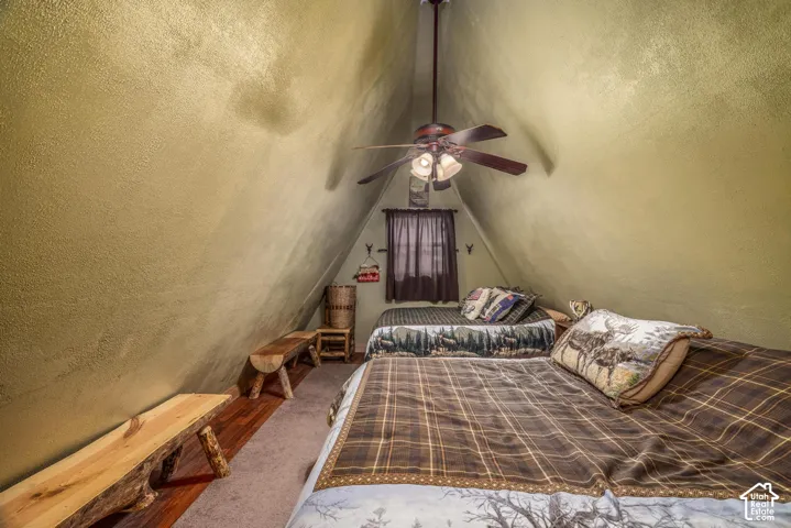 A-frame interior featuring vaulted angled walls, wood-finish flooring, and a ceiling fan with integrated lighting